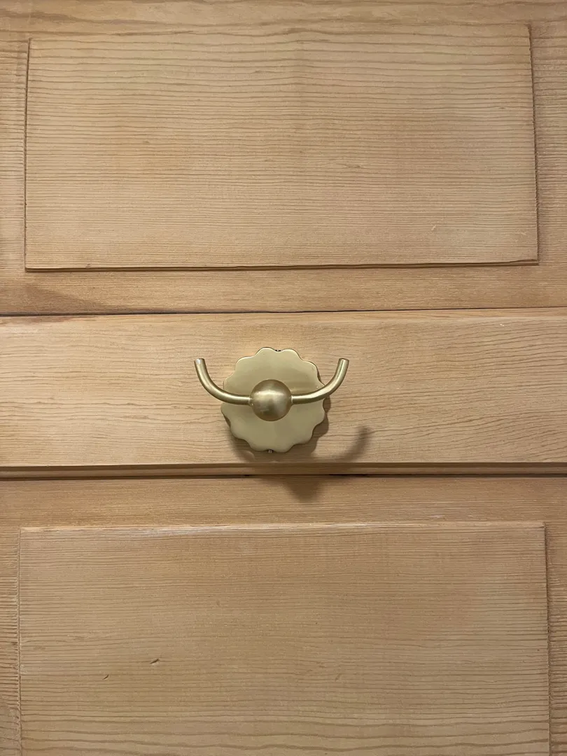 A gold double-hook mounted on a wood-paneled cabinet.