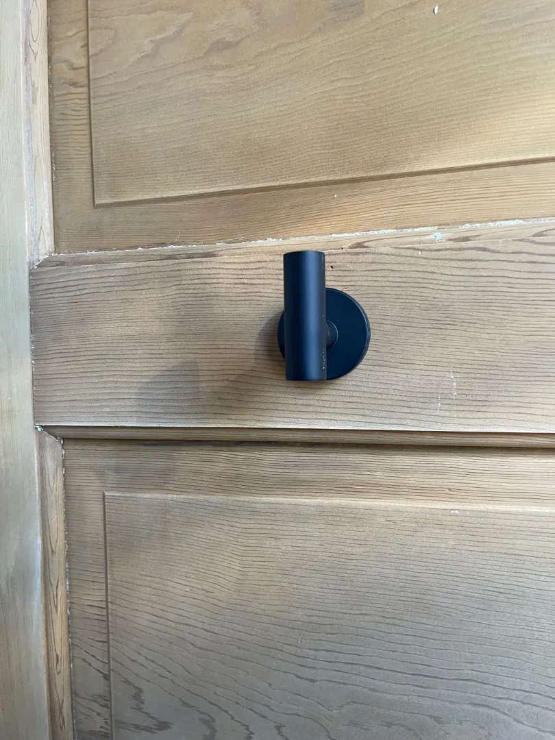 A black wall hook mounted on a wood-paneled surface.