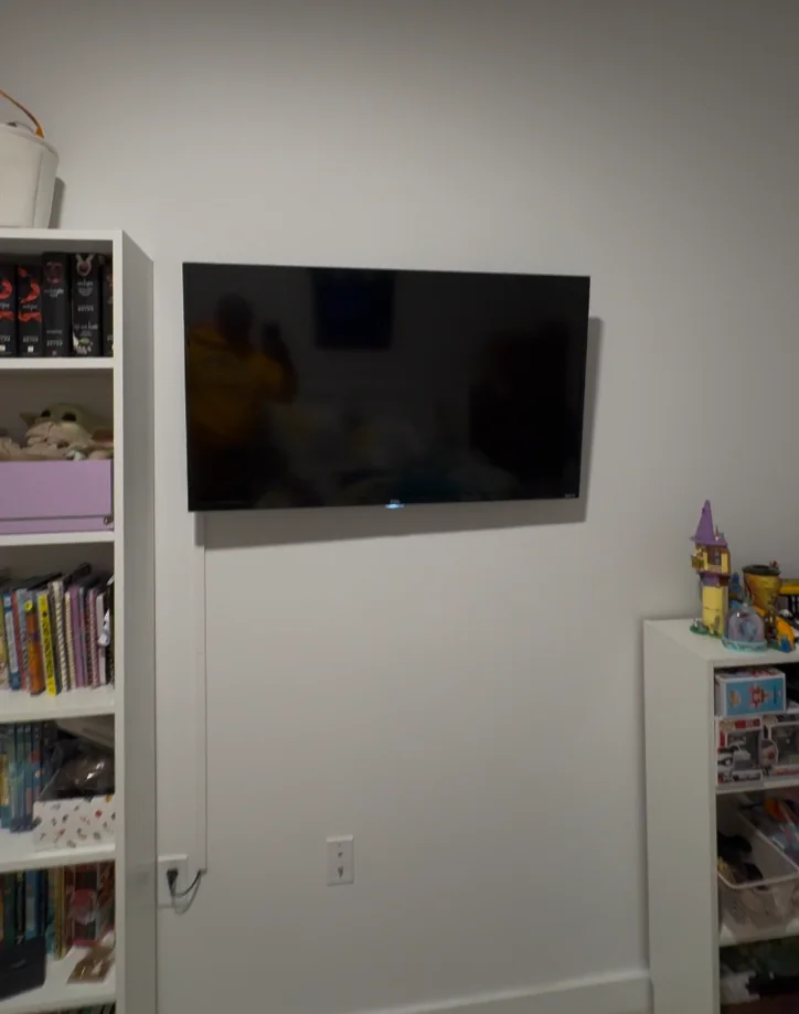 Small TV mounted on wall in kids room with bookshelves and toys